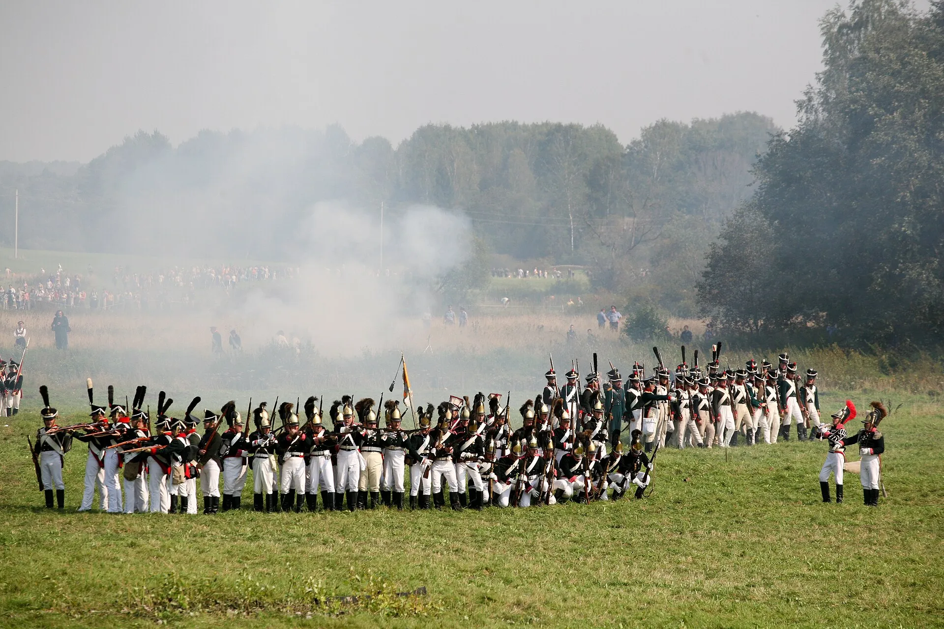 Реконструкторы в мундирах 1812 года дают залп на Бородинском поле, вдали зрители