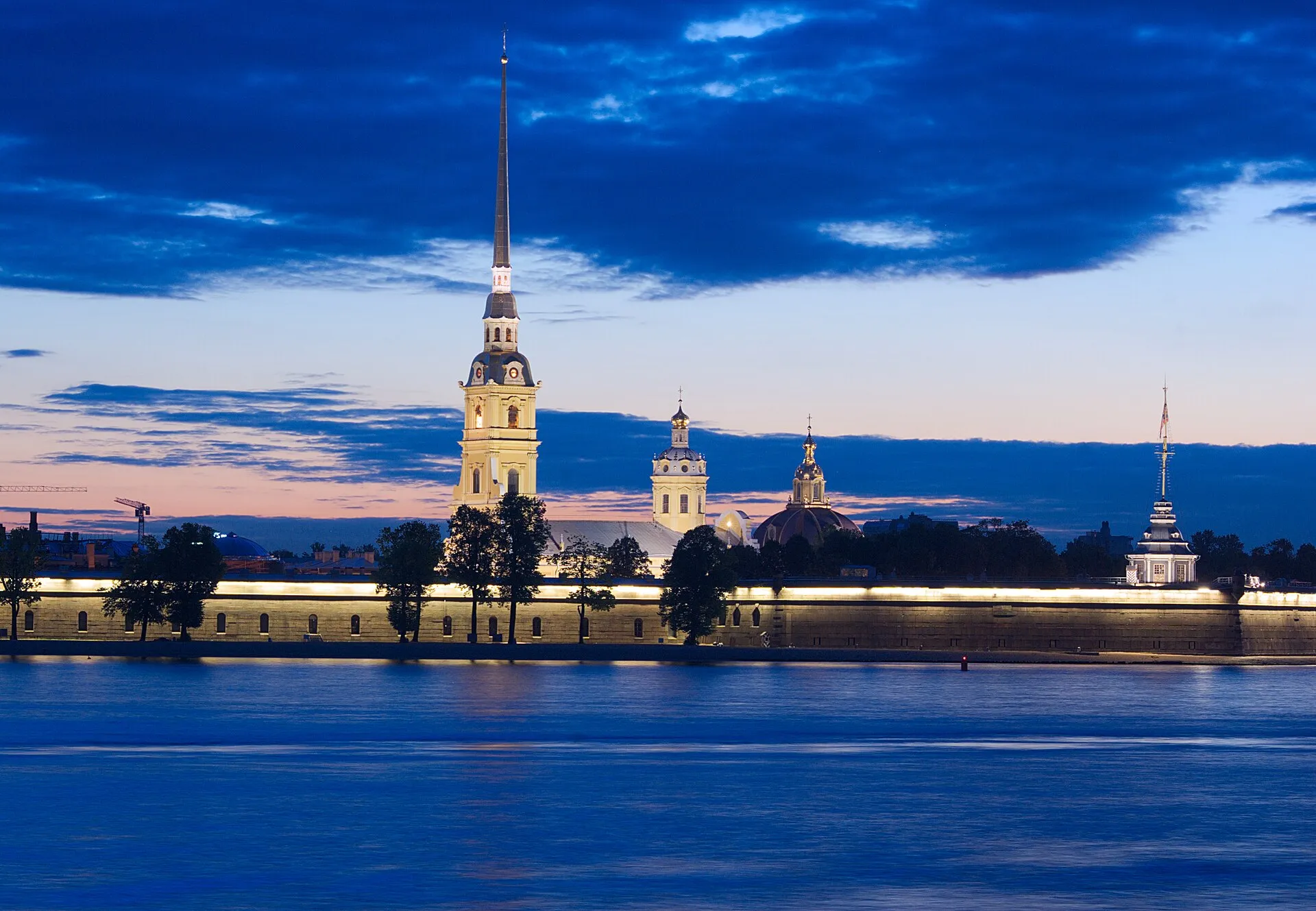 Петропавловская крепость вечером с подсвеченными стенами, вид через Неву