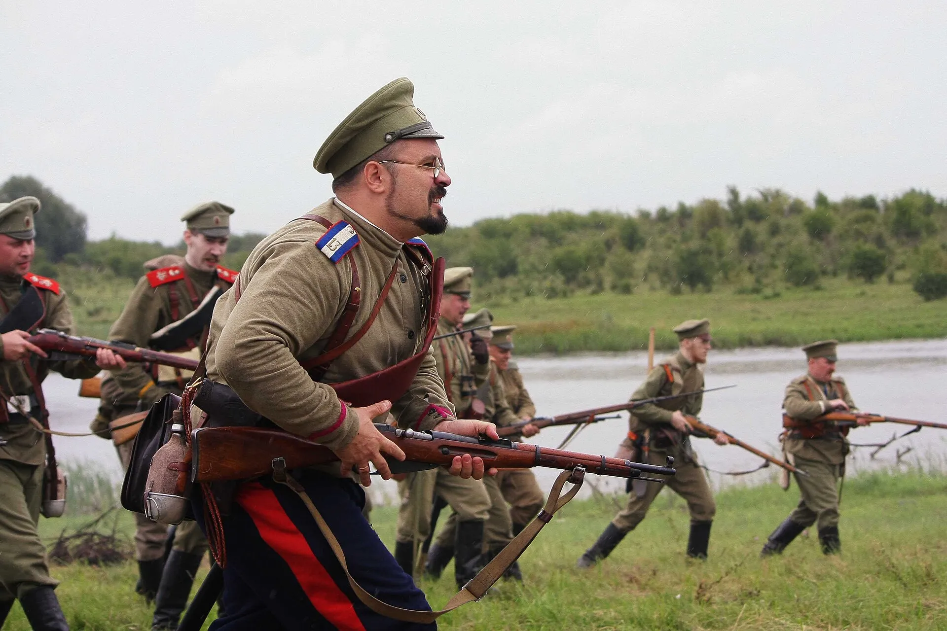 Реконструкторы в форме русской армии 1914 года идут в атаку с винтовками на поле у Совхозного